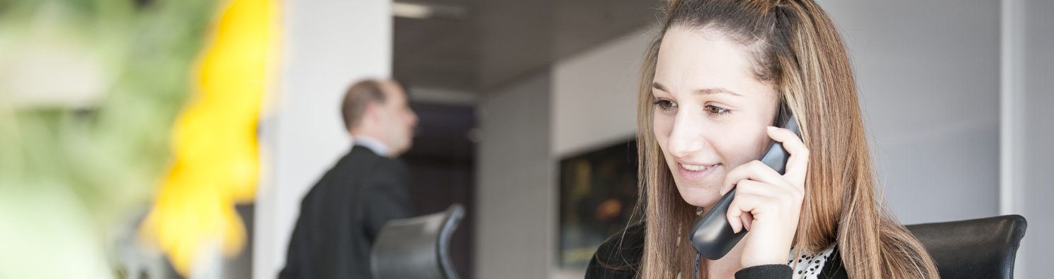 Young woman at reception desk holding telephone.