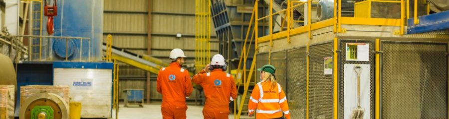 Three people in safety gear walking through factory