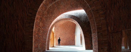 Man standing at the end of a long semi-circular corridor of bricks at Imperial Kiln Museum, China