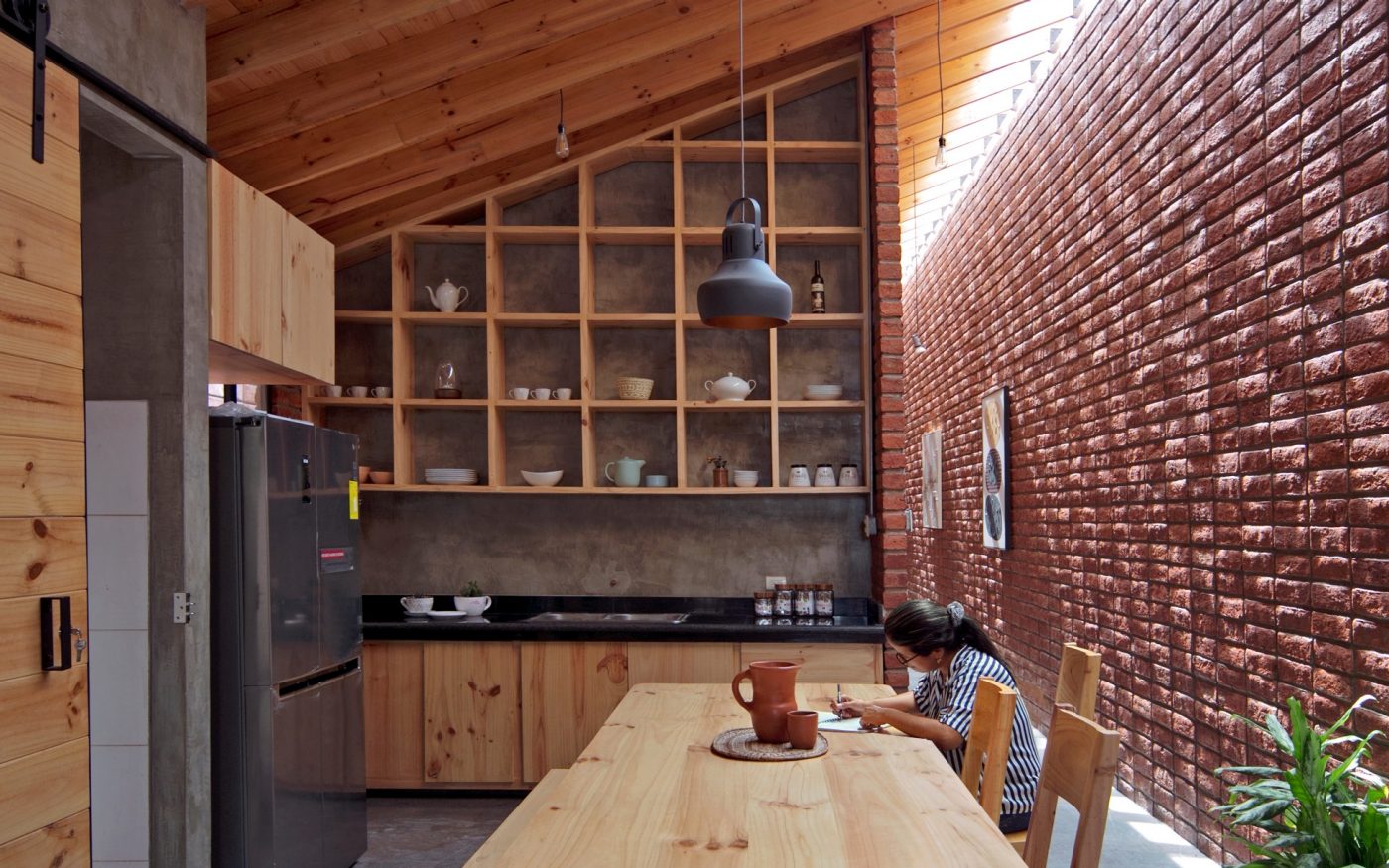 Woman sitting in modern kitchen with brick wall and wooden cupboards