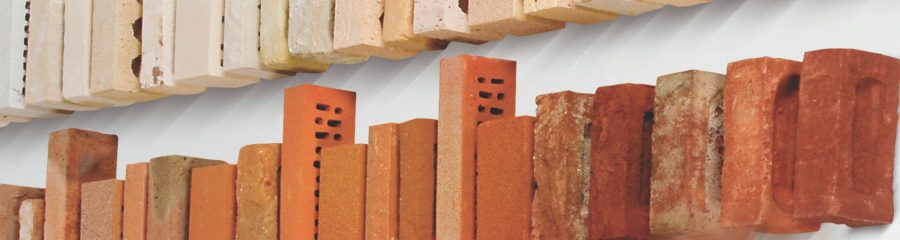 Hand picking sample brick from a row of clay bricks