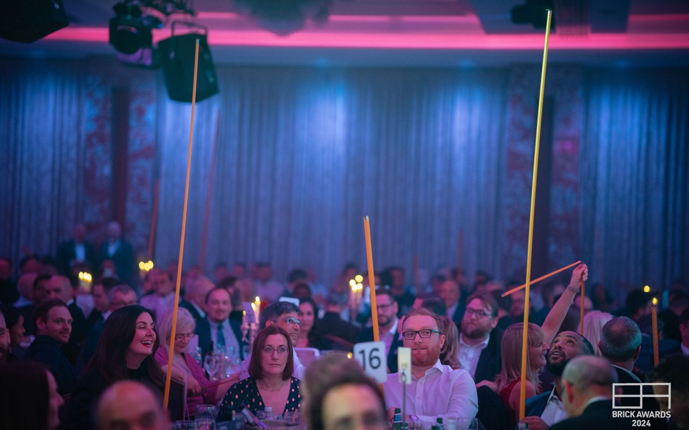 Photo of the blue/puple lit room with many people sat round tables
