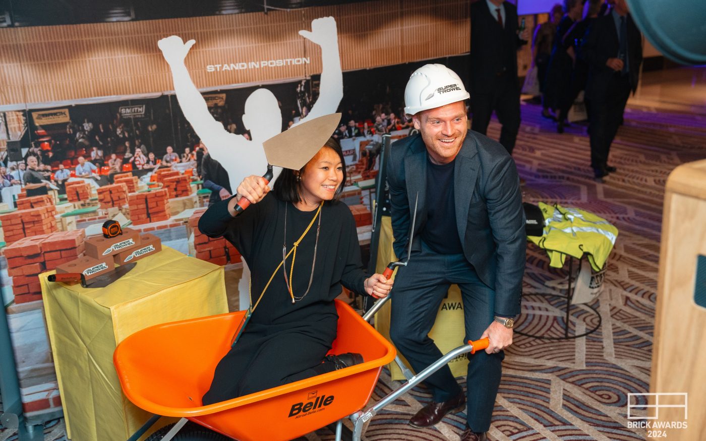 two people playfully posing with wheelbarrow and hard hat