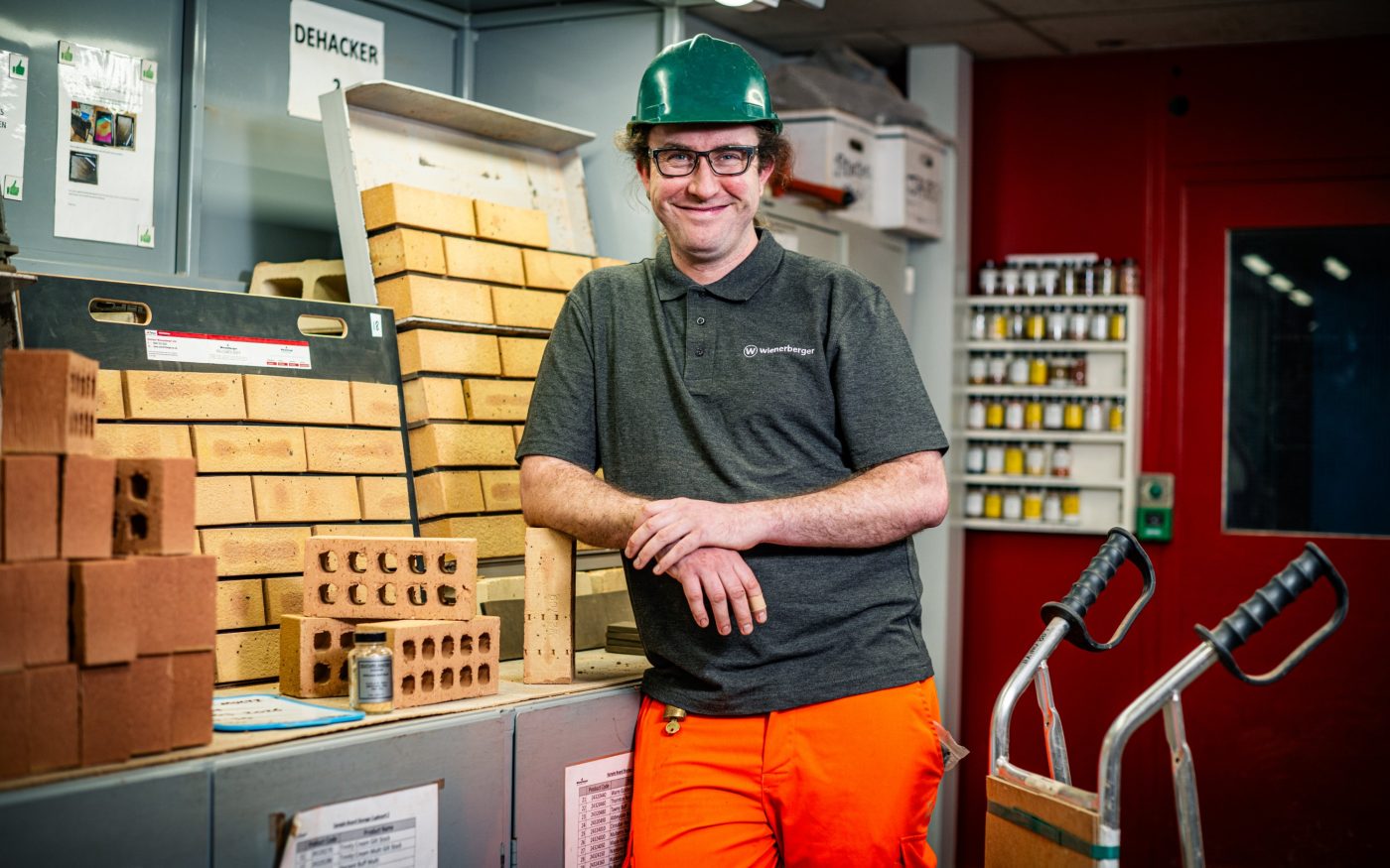 Image of a man in a hard hat smiling into camera next to bricks