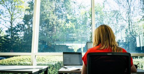 Cheadle Head Office, Women in red top sat at desk looking out the windows at tree