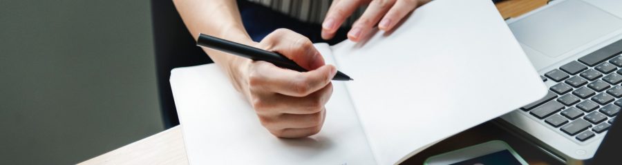 Hands holding a pen and writing in a notebook