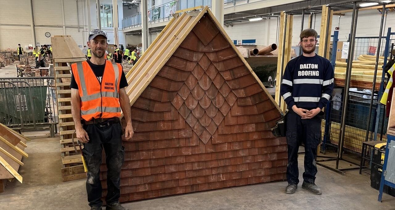 Two roofing students standing beside roof