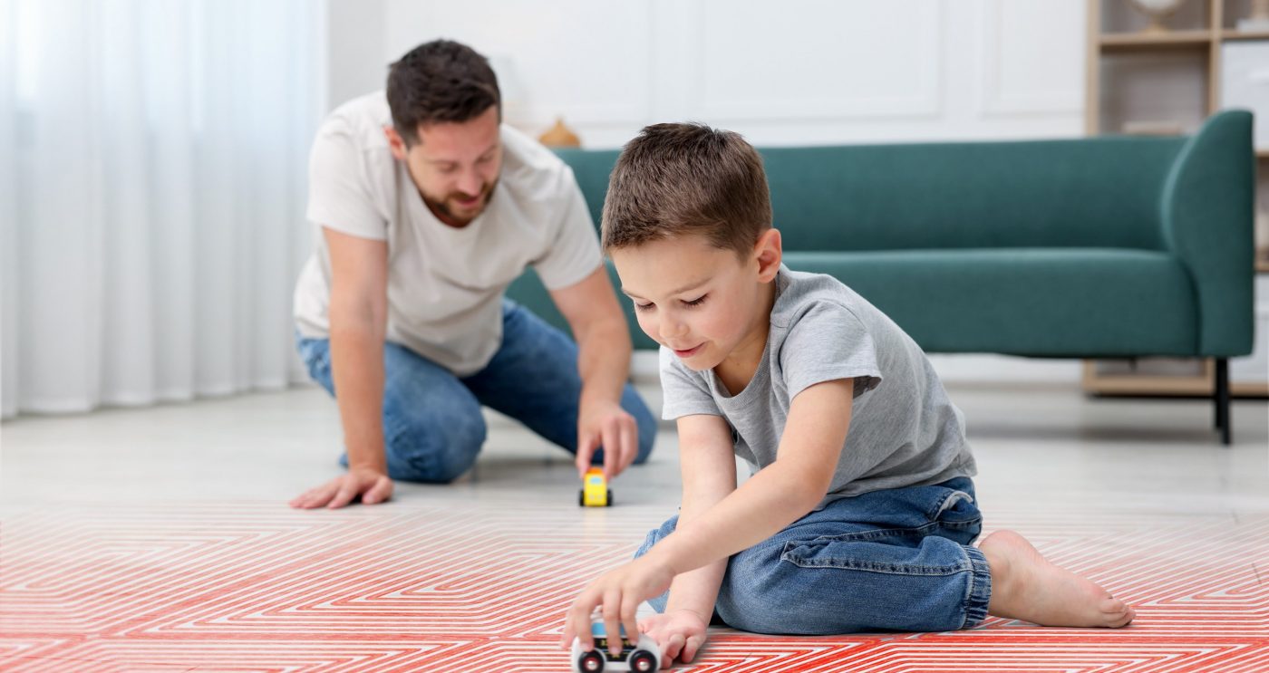 Father and son playing on warm floor at home, double exposure with underfloor heating system