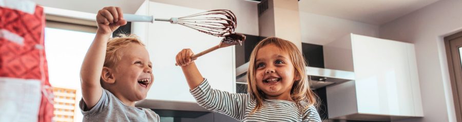 Two children baking in a kitchen smiling and laughing