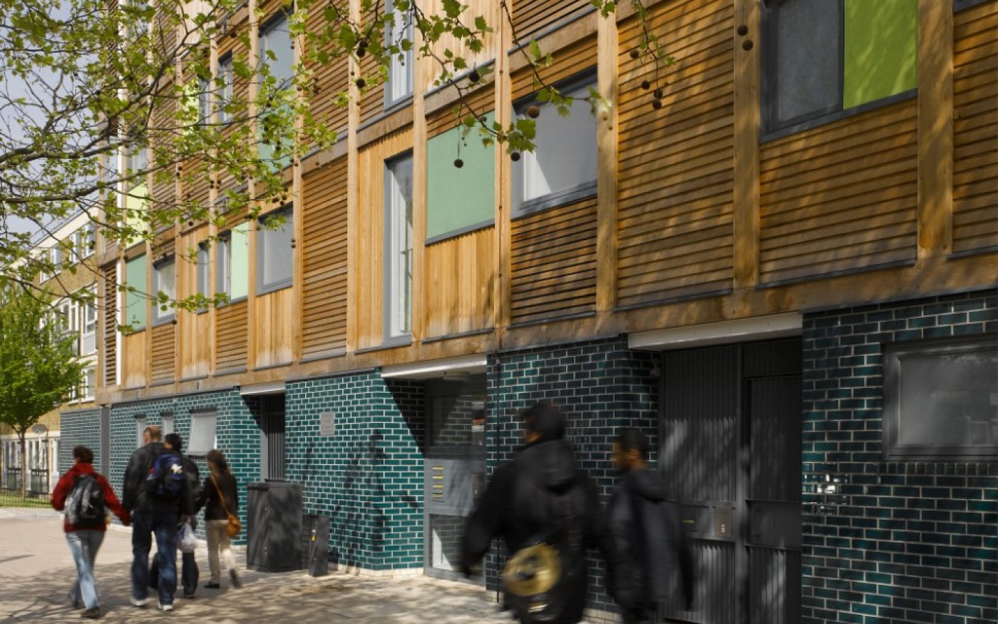 Pedestrians walking past modern apartment building with green glazed brick facade