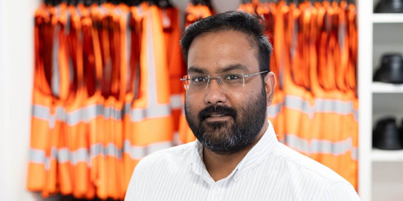 Man looking towards the camera with a rail of hi vis vests behind him