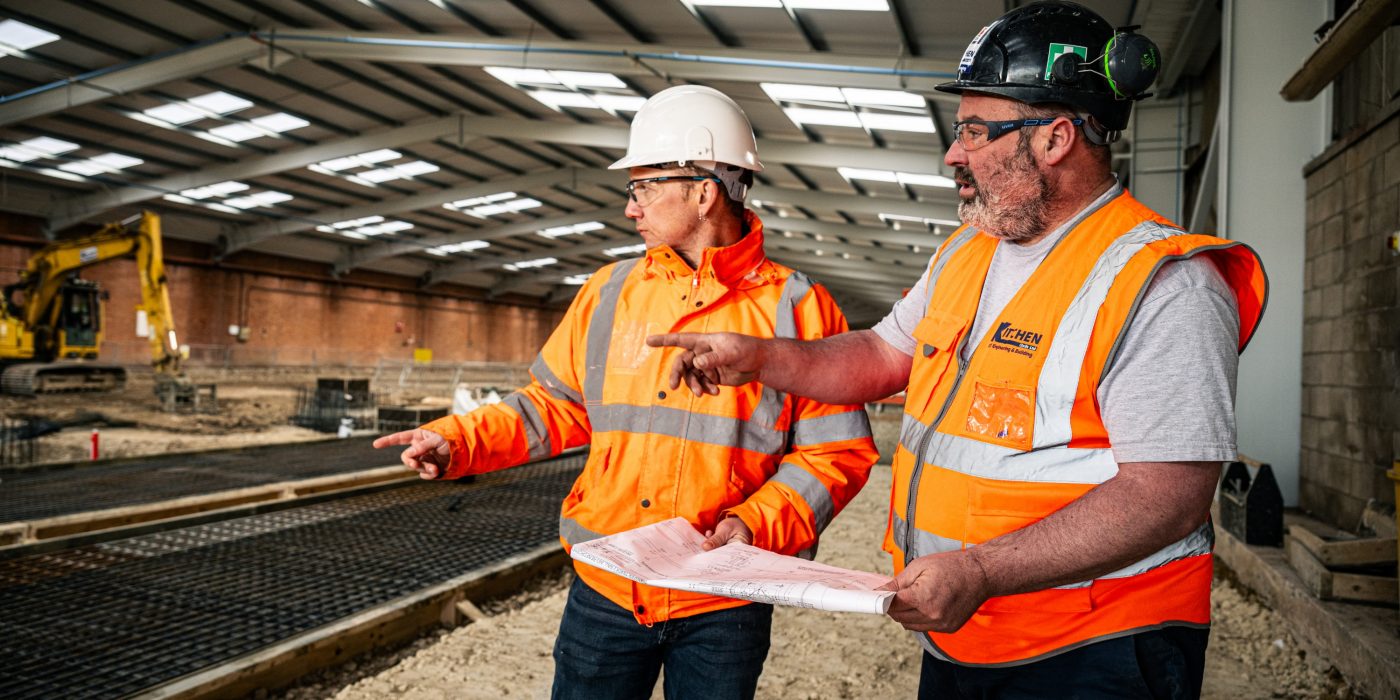2 people in the factory in full PPC looking at something to their left