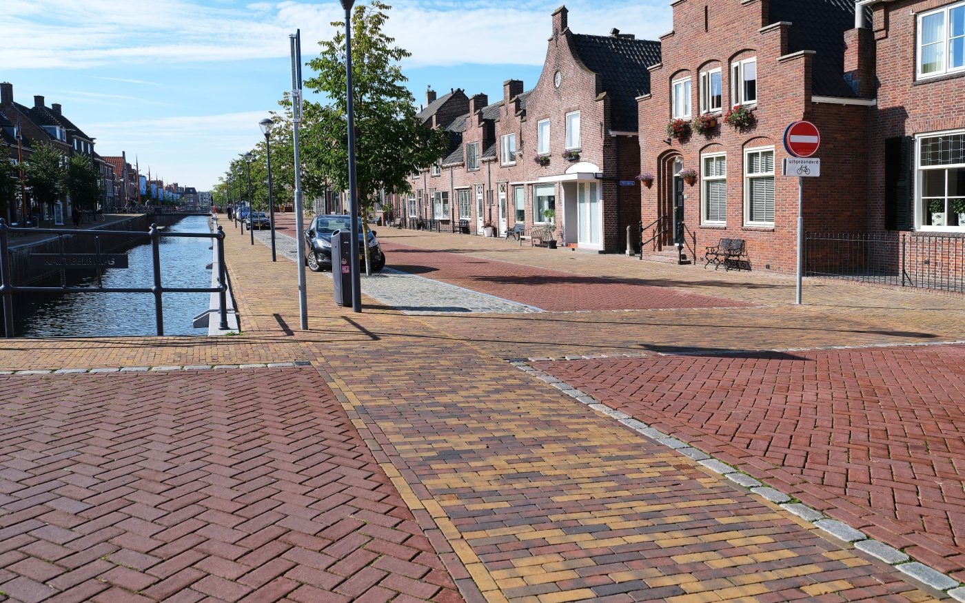 Clay paved path with buildings on right and trees in front