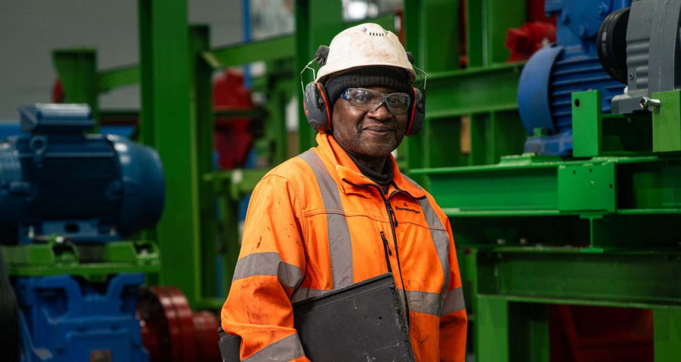 Man in the factory wearing white helmet, goggles and ear defenders