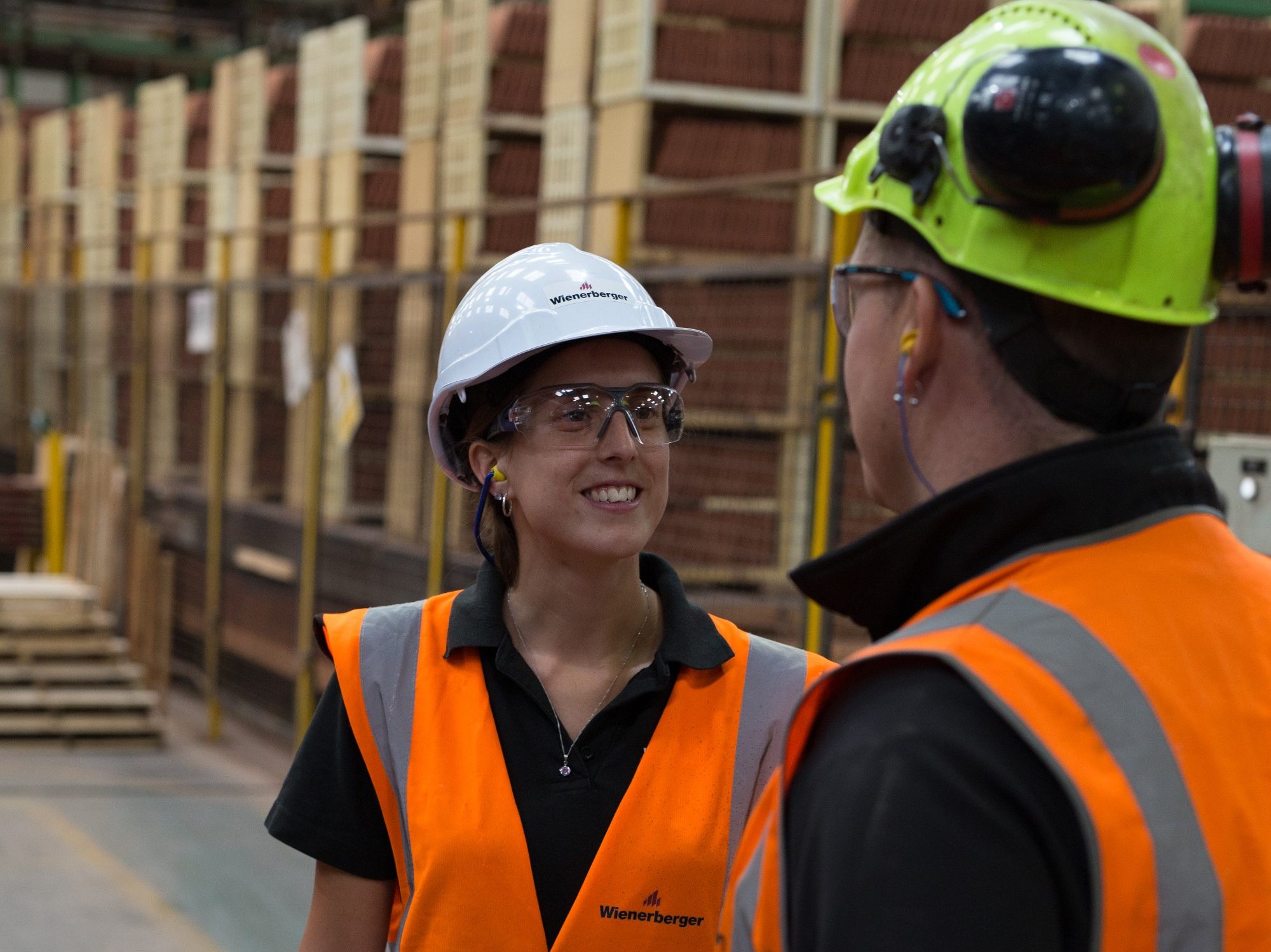 Woman in safety wear smiling at colleague in factory