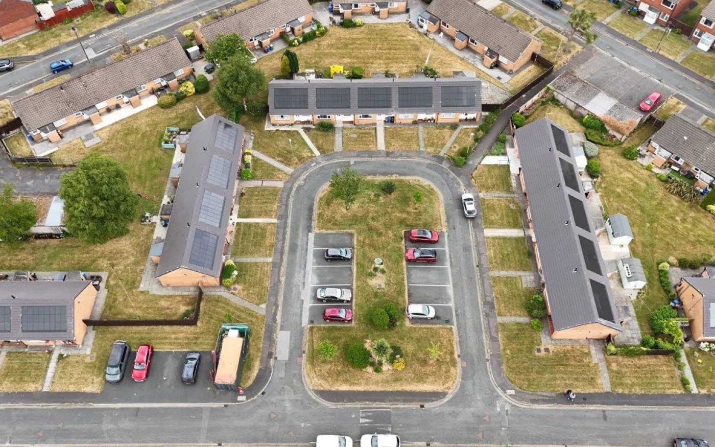 Aerial view of single-story houses with dark roofs and solar panels around a central parking loop