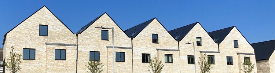 Row of modern cream brick terraced houses with row of trees and blue sky