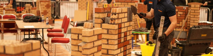 Man using a trowel to tidy up a brick wall he has constructed during a competition