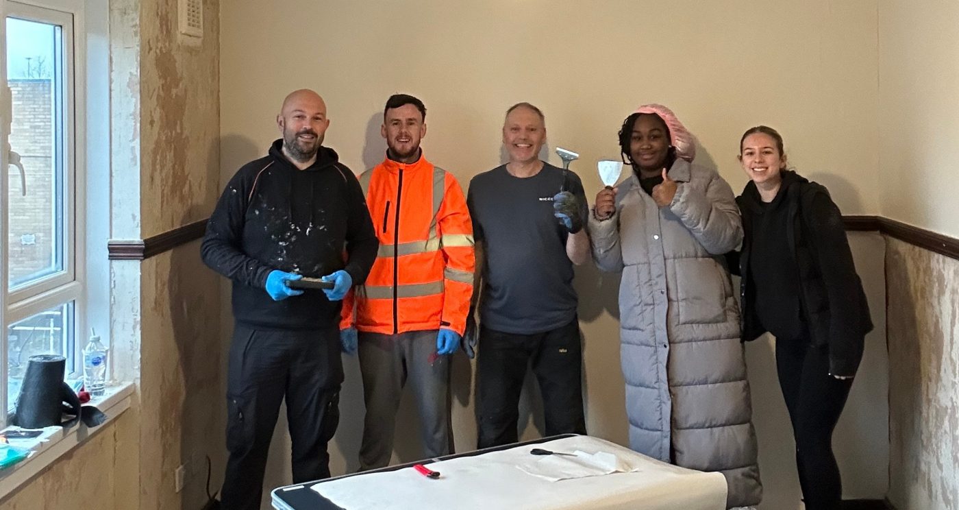 5 volunteers smiling at the camera whilst decorating a room