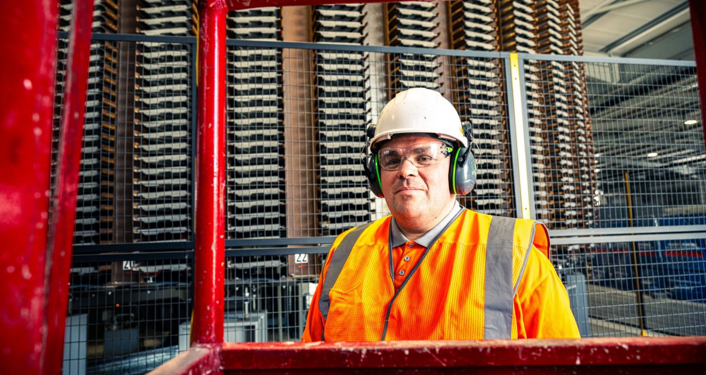 Man in safety equiptment smiling at the camera in a factory