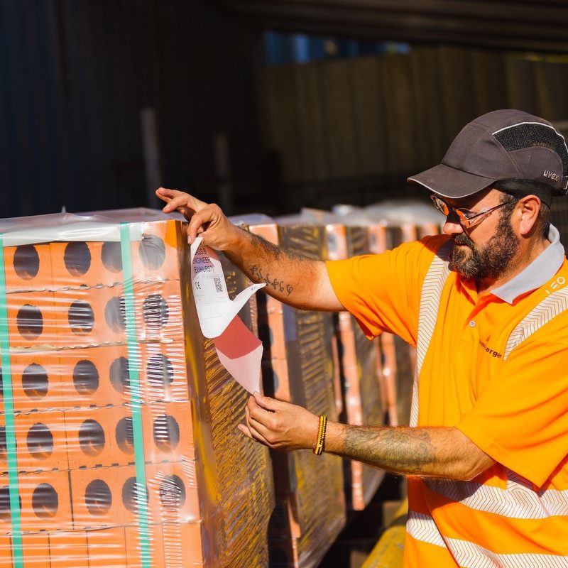 Man in high viz clothing putting sticker on pallet of bricks