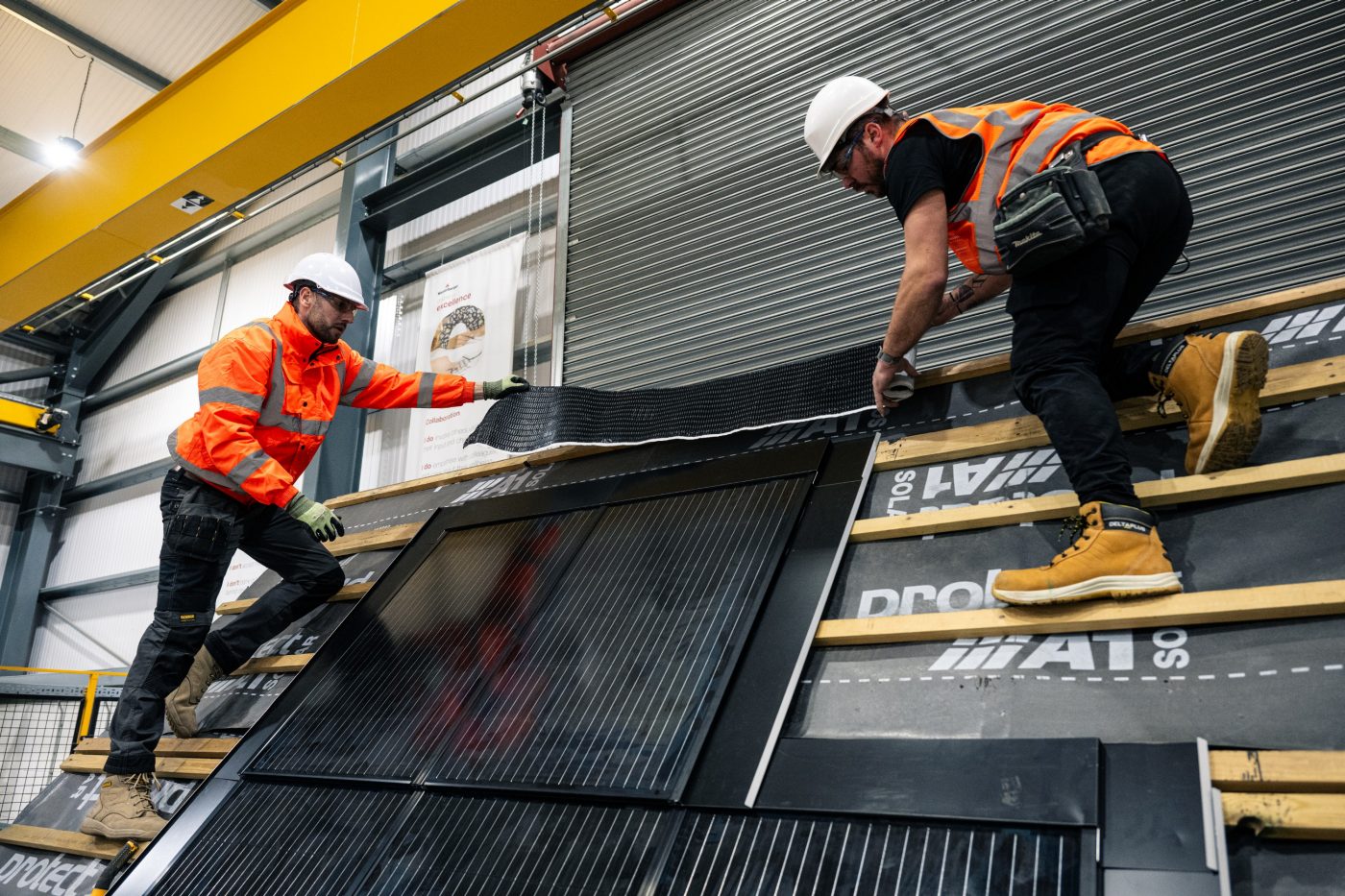 Two men working on a demo roof in a factory installing in-roof solar