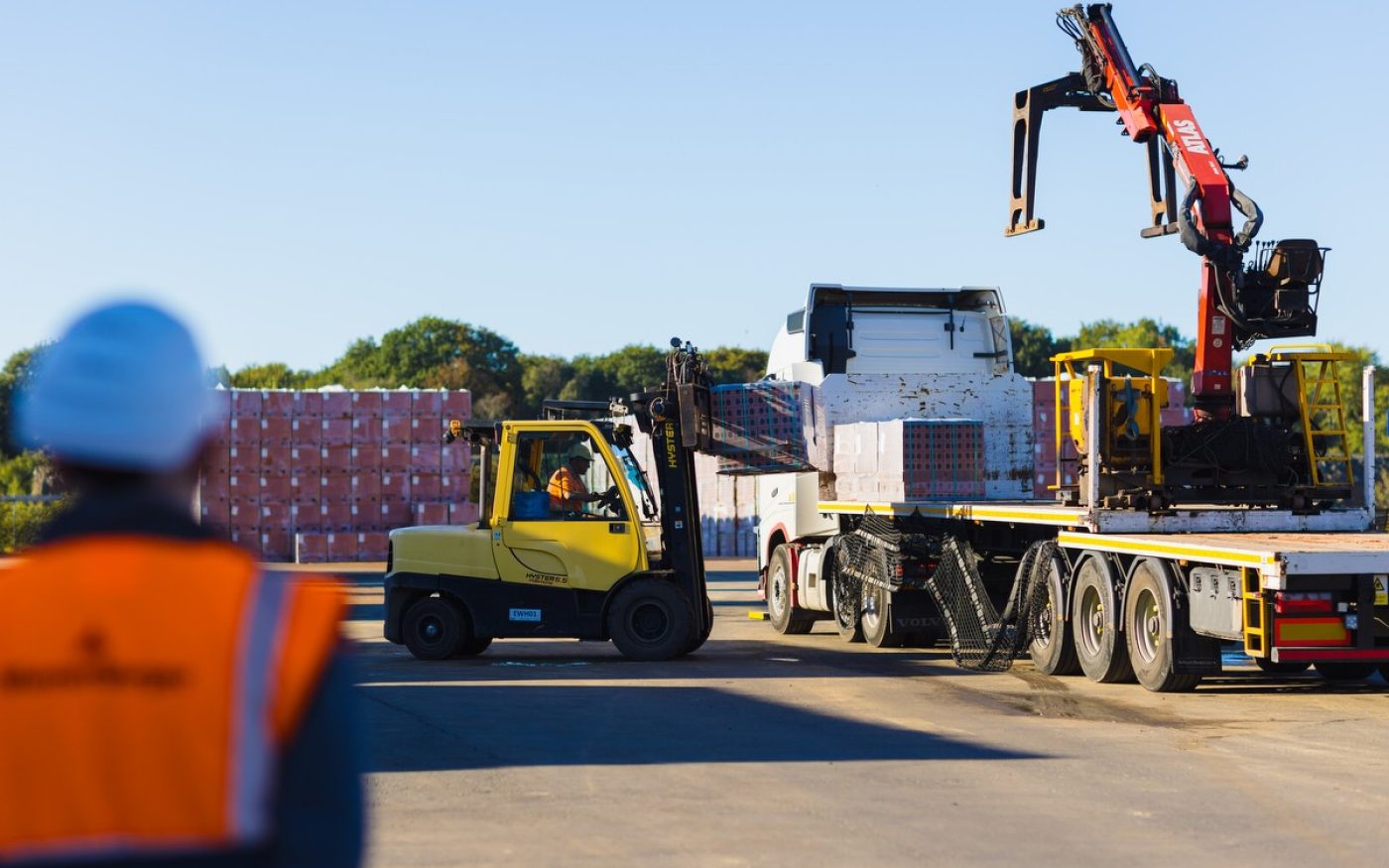 Man watching brick pallets being loaded onto flatbed lorry