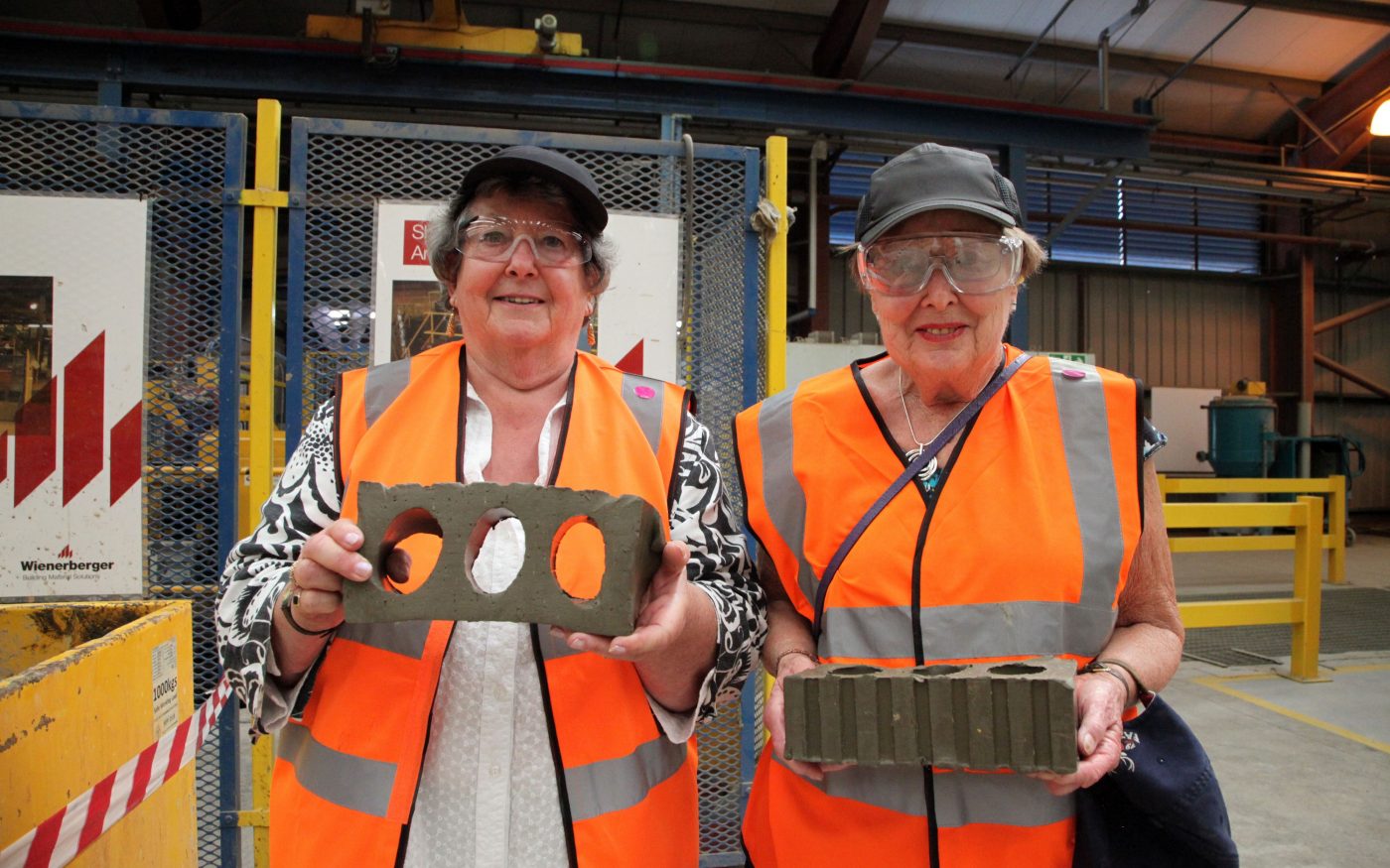 Two women in PPE holding clay bricks