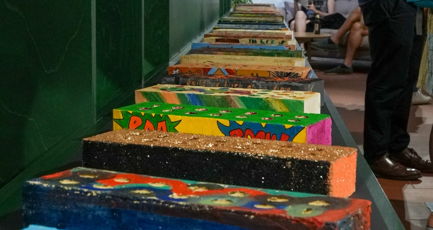 Blue and white brick with red swirled surrounded by visitors admiring decorated bricks