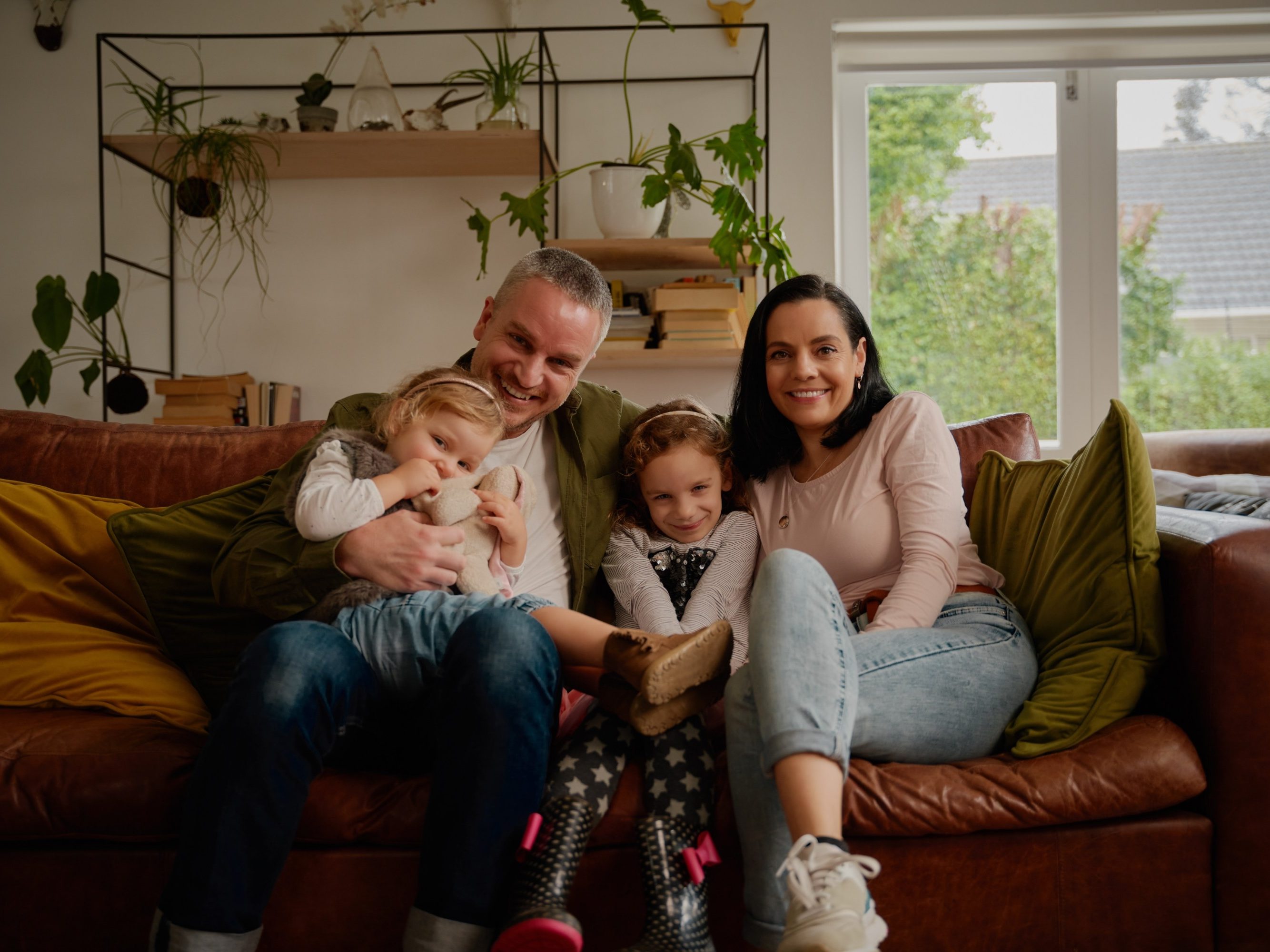 Cheerful couple sitting on couch with two beautiful little daughters at home - one big happy family portrait on a modern couch at home
