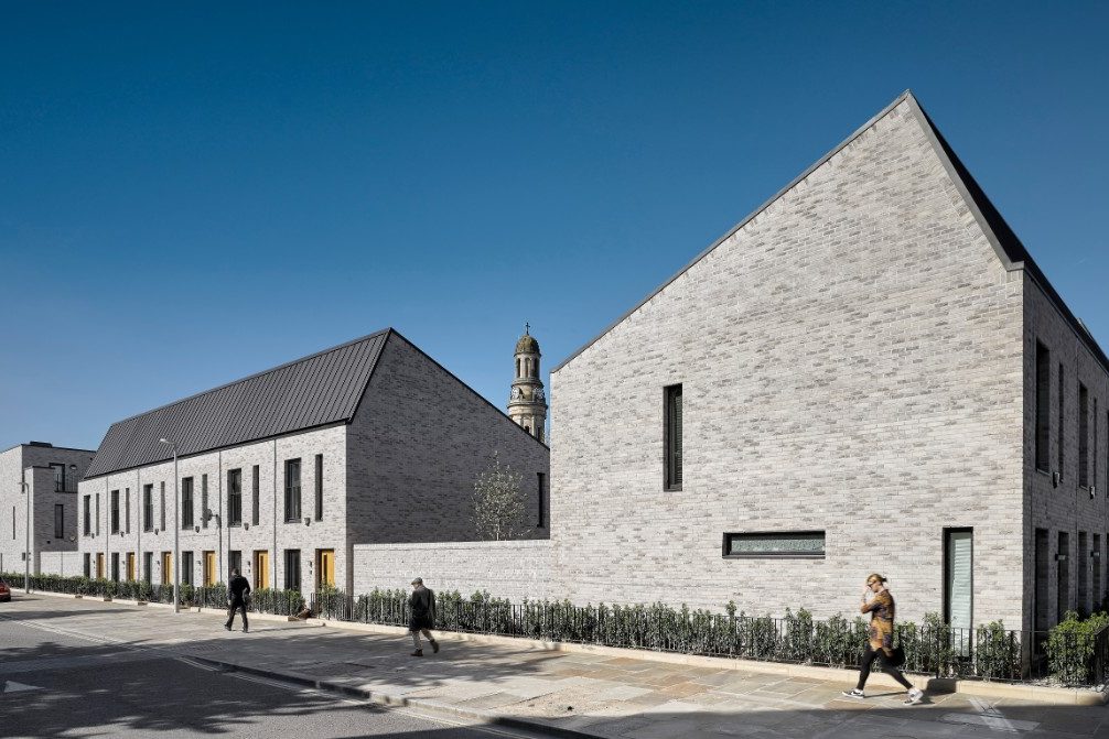 Pedestrians walking past modern grey brick terraced houses