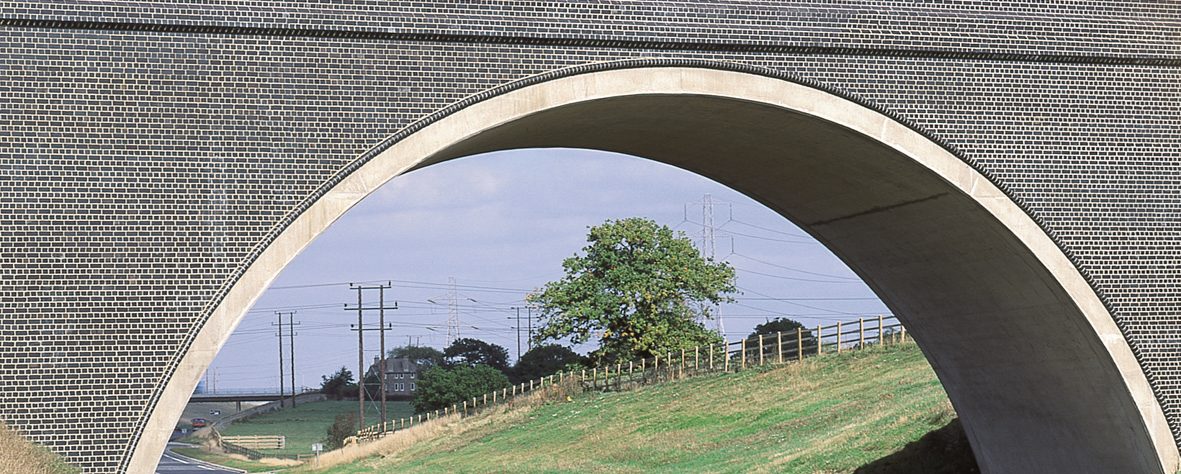 Bridge over road with green hill and tree