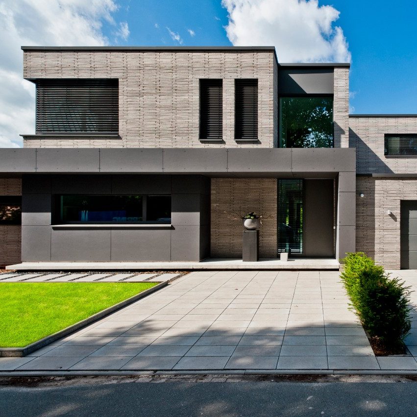 Large red brick detacahed home with blue sky and front lawn