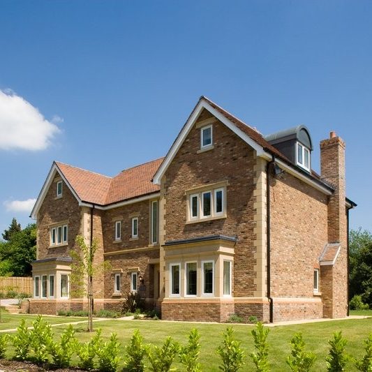 Large red brick detacahed home with blue sky and front lawn