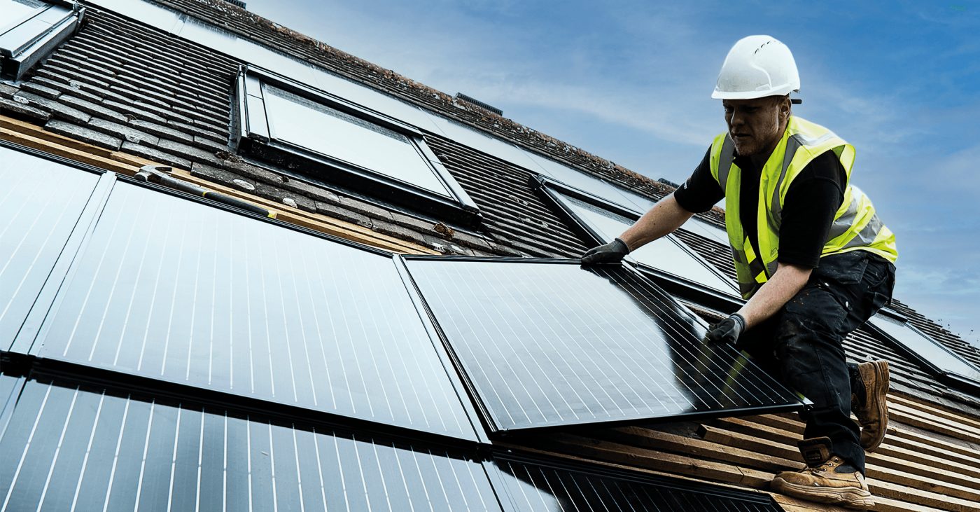 Man in hard hat laying in-roof solar panel on roof
