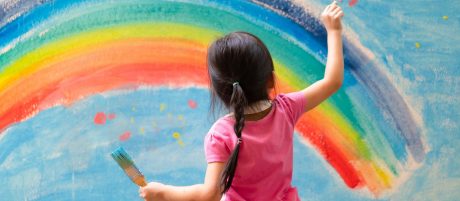 Little girl painting a rainbow on a wall