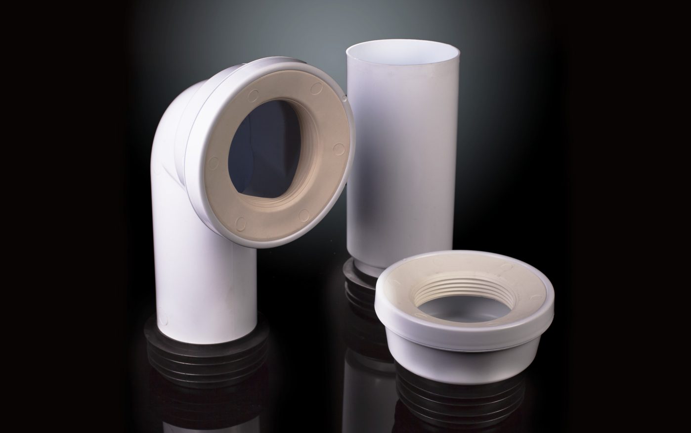 Assorted white PVC pipe fittings standing upright on a reflective surface