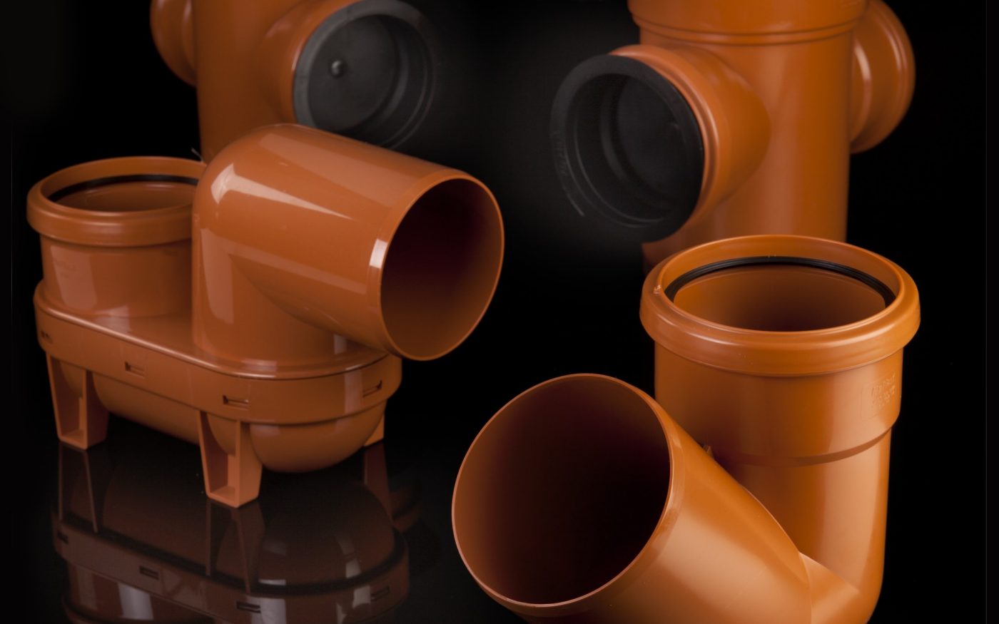 Variety of brown plastic drainage fittings arranged on a black surface.