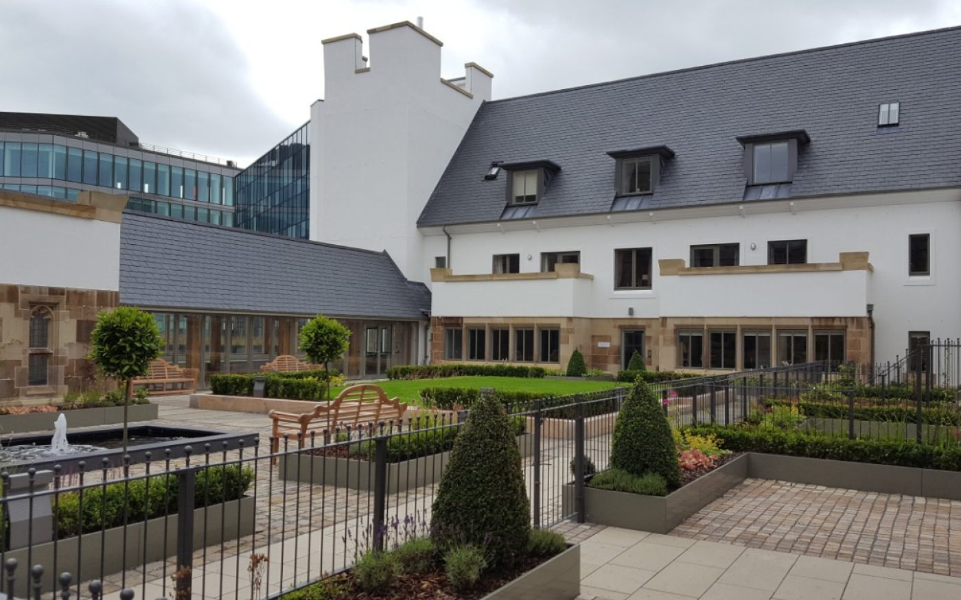 White and brick building with grey roof and gardens outside