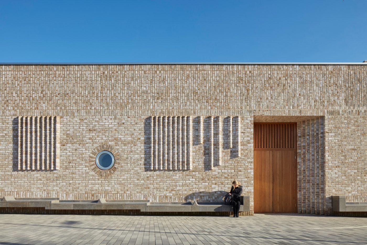 Woman sitting outside modern brick building with large wooden door