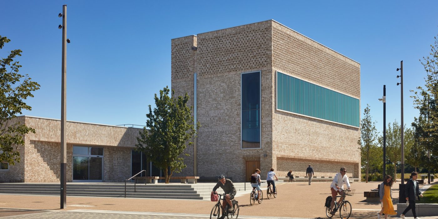 Modern brick building with paved area, pedestrians and cyclists travelling
