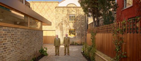 Gilbert and George stood next to each other in matching suits in the courtyard of the building