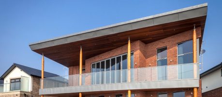 Brick two storey property with glass balcony and blue sky behind