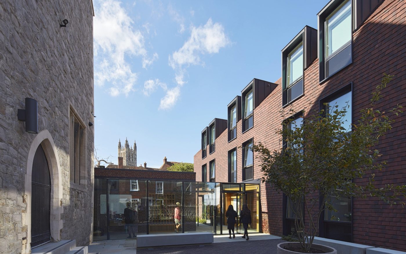 Courtyard between historic medieval building and ultra-modern accommodation block, with church tower in far distance