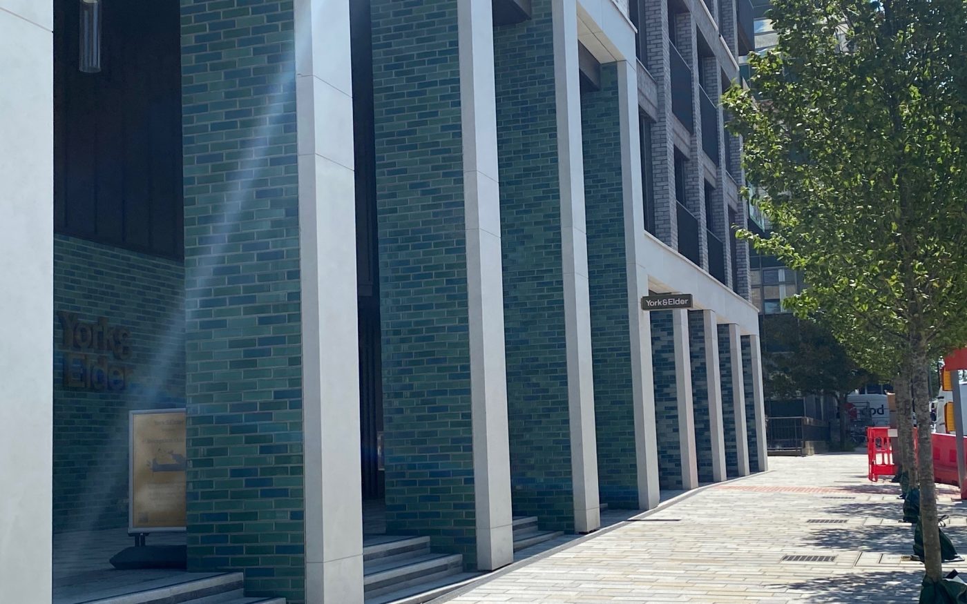 Green and blue glazed bricks on modern apartment building entrance with trees on the right side