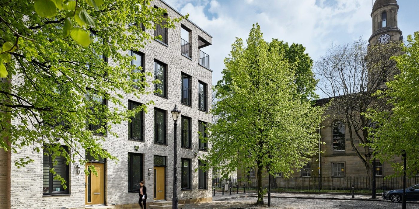 Trees outside modern brick terraced houses next to old church