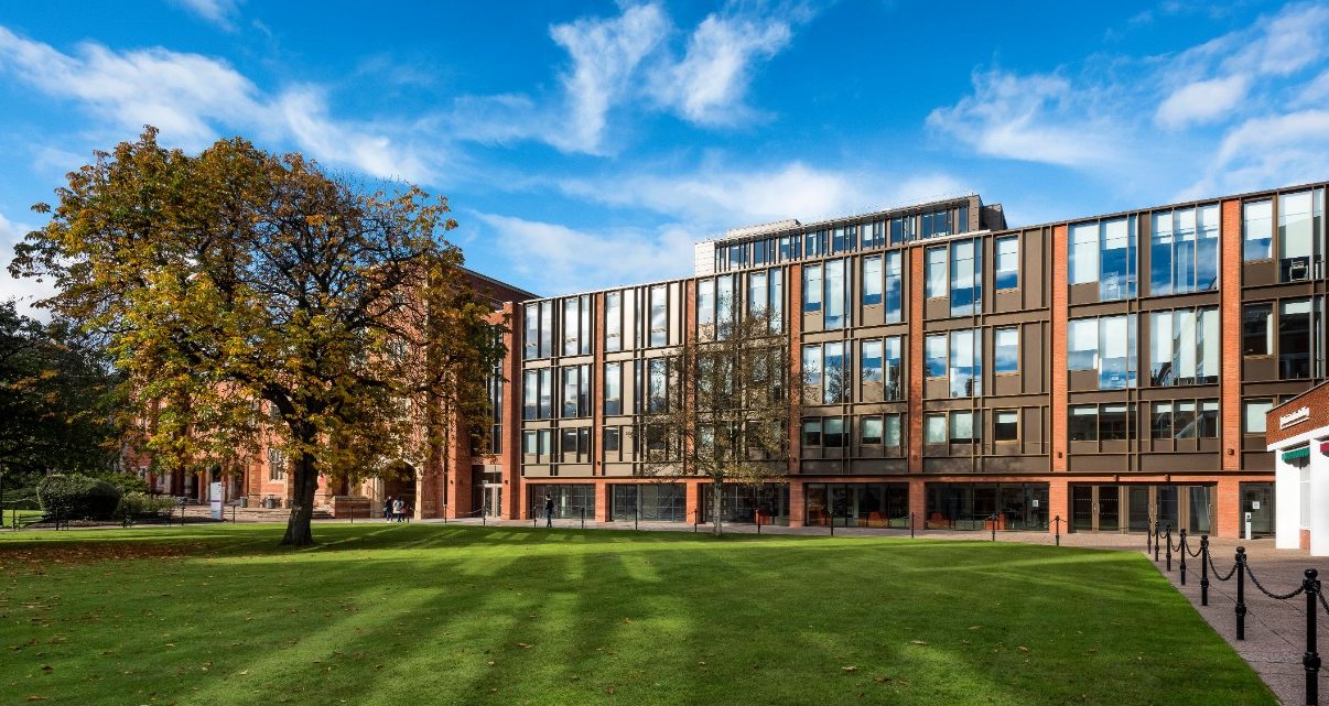 Large brick university building with grass lawn, trees and blue sky