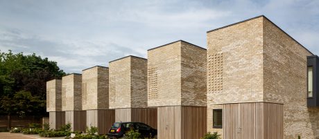 Ultra modern terraced houses with brick walls and large window, fronted with paved driveways and lawns