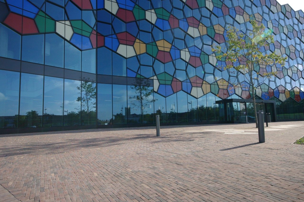Clay paved outside space in front of large modern building with multi-coloured glass windows