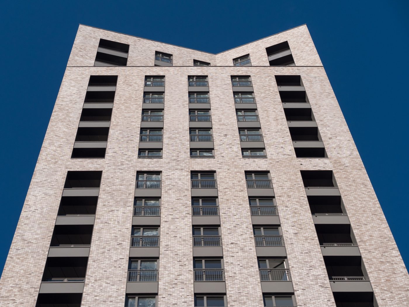 Looking up at modern high-rise building with brick facade against blue sky